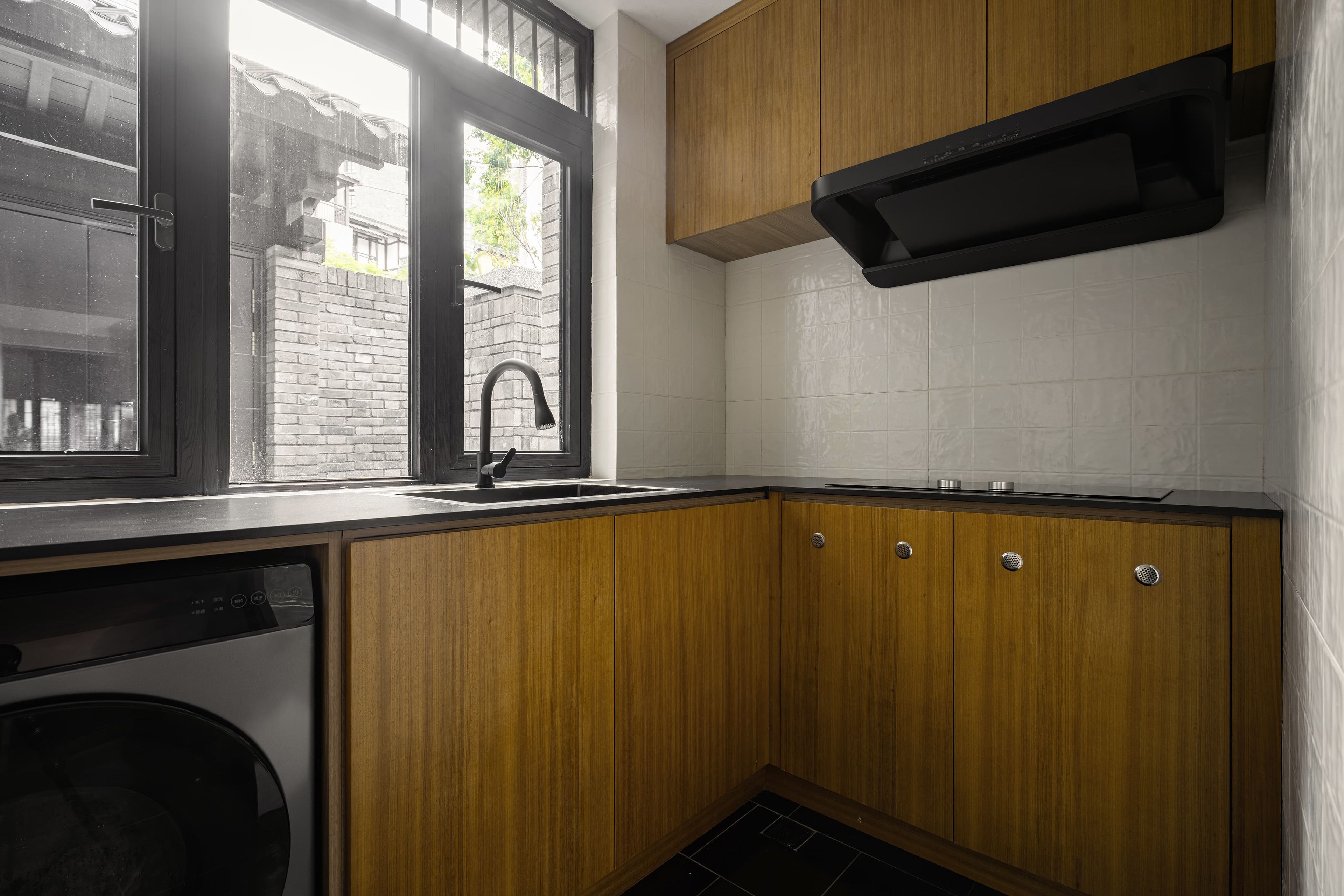 Una cocina con armarios de madera, un grifo negro y una ventana con vista a un edificio de ladrillo.