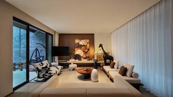Una sala de estar moderna con un sofá grande, una mesa de centro y un televisor. Hay un ventanal con vista a un muro de ladrillo y una silla colgante afuera.