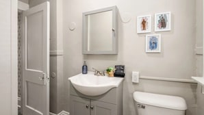 Un bagno con lavandino, specchio e water bianchi. Tre quadri appesi alla parete.