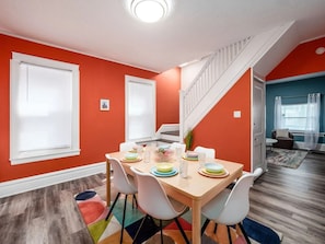Ein Essbereich mit einem Holztisch, gedeckt für vier Personen, umgeben von weißen Stühlen, in einem Raum mit orangefarbenen Wänden und einer Treppe.
