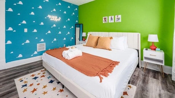 Una camera d'albergo con un letto, un comodino, una lampada e una parete decorata con motivi a nuvole.