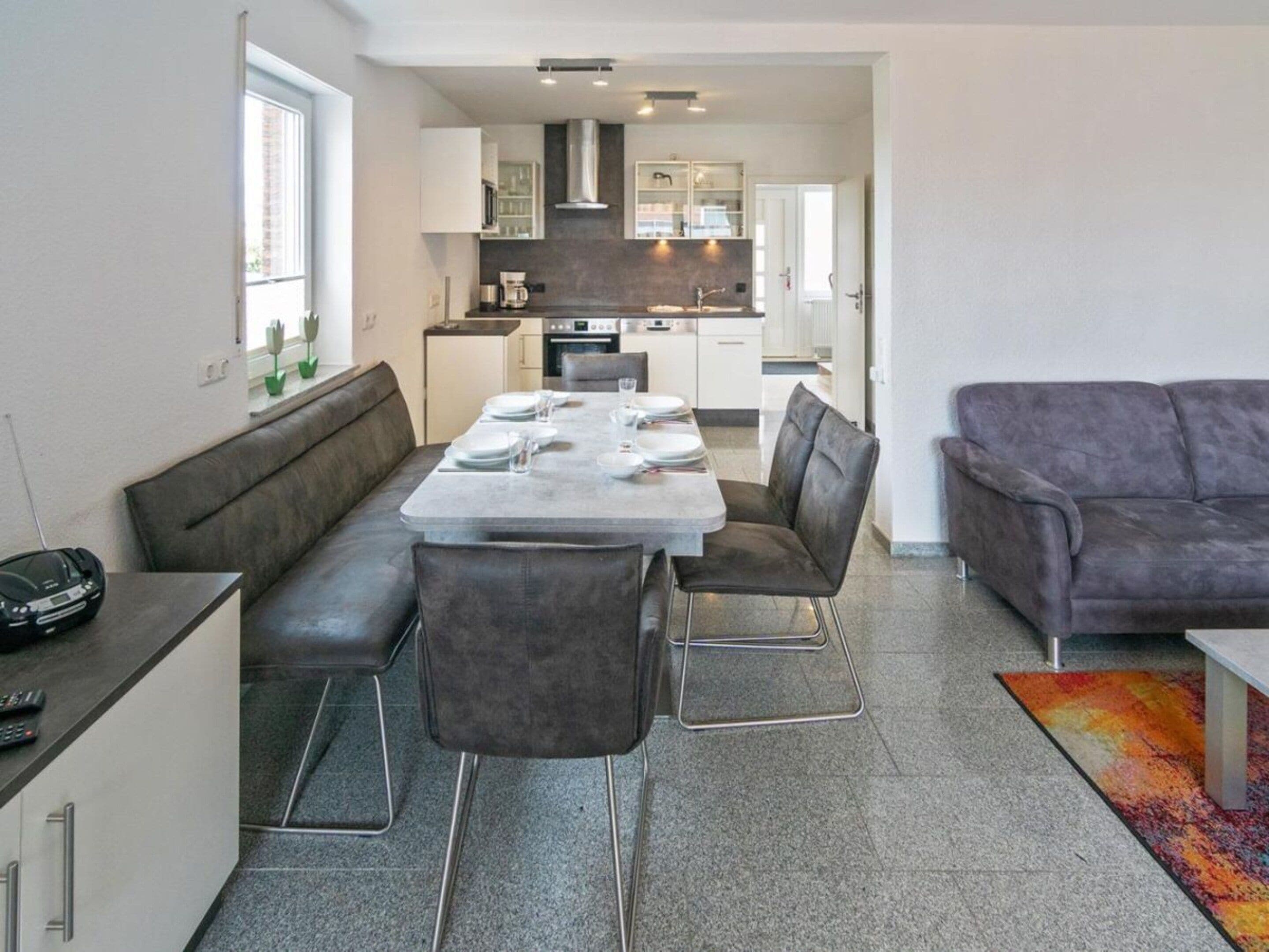 Un salon moderne avec un coin repas, des canapés gris, une table basse et une cuisine en arrière-plan.