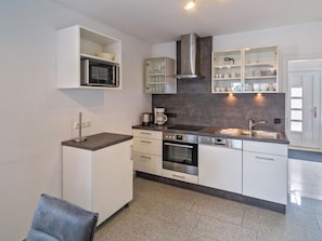 Een moderne keuken met witte kasten, een ingebouwde magnetron, een roestvrijstalen afzuigkap en een koffiezetapparaat.