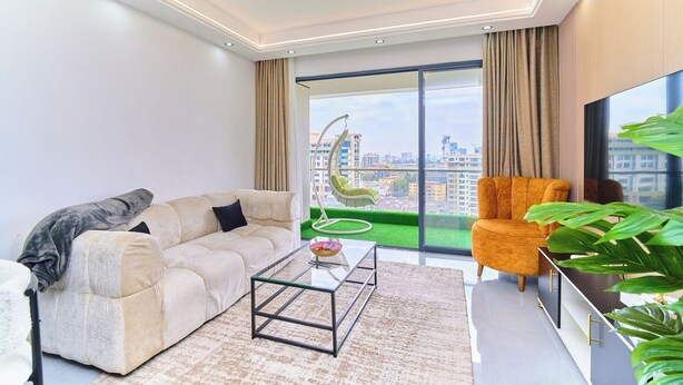 A modern living room with a sofa, armchair, and coffee table, large windows with a city view, and a balcony with greenery. - Charming apartment in beautiful Kilimani, Nairobi perfect for your stay (Nairobi)