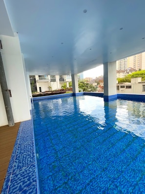 A swimming pool with clear blue water, surrounded by a tiled deck and white walls. - Charming apartment in beautiful Kilimani, Nairobi perfect for your stay (Nairobi)