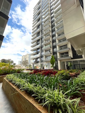 A modern high-rise building with multiple balconies and a landscaped garden area with various plants. - Charming apartment in beautiful Kilimani, Nairobi perfect for your stay (Nairobi)