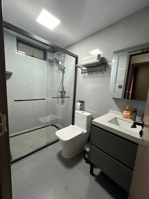 A modern bathroom with a glass-enclosed shower, a toilet, a sink with a soap dispenser, and a mirror above the sink. - Charming apartment in beautiful Kilimani, Nairobi perfect for your stay (Nairobi)