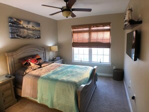 A bedroom with a bed, a nightstand, a lamp, a ceiling fan, a window with blinds, and a wall-mounted TV. - Lovely townhome in the popular Villages of Five Points (Lewes)