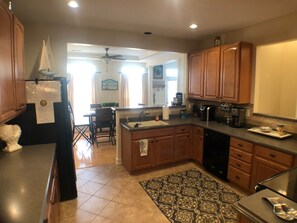 A kitchen with wooden cabinets, a black refrigerator, a coffee maker, and a dining area with a table and chairs. - Lovely townhome in the popular Villages of Five Points (Lewes)