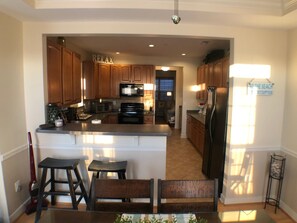 A kitchen with wooden cabinets, a central island with stools, a microwave, and a refrigerator. - Lovely townhome in the popular Villages of Five Points (Lewes)