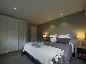 A bedroom with a bed, bedside lamps, a door, and a nightstand.