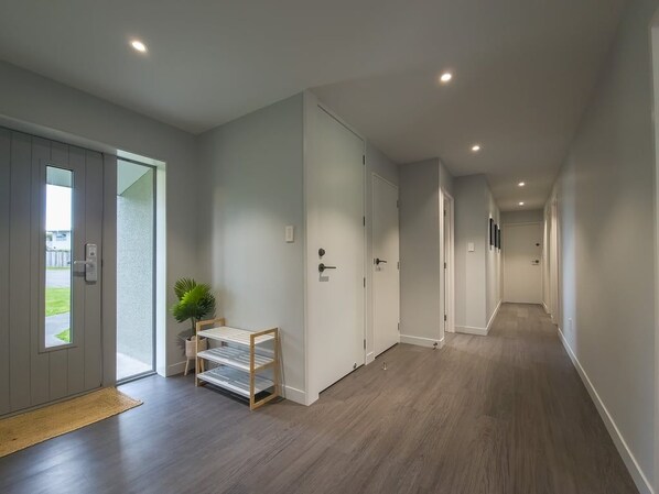 A hallway with a wooden floor, white walls, and a door leading to a garden.