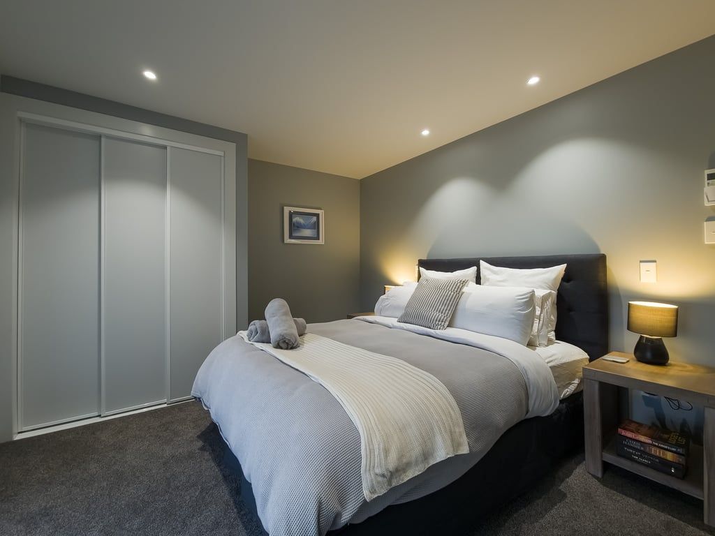 Een slaapkamer met een bed, nachtkastje, lamp en een kledingkast.