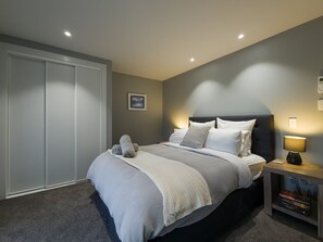 A bedroom with a bed, bedside table, lamp, and a wardrobe. - Beachside Bliss - Two Bedroom Apartment (Napier)