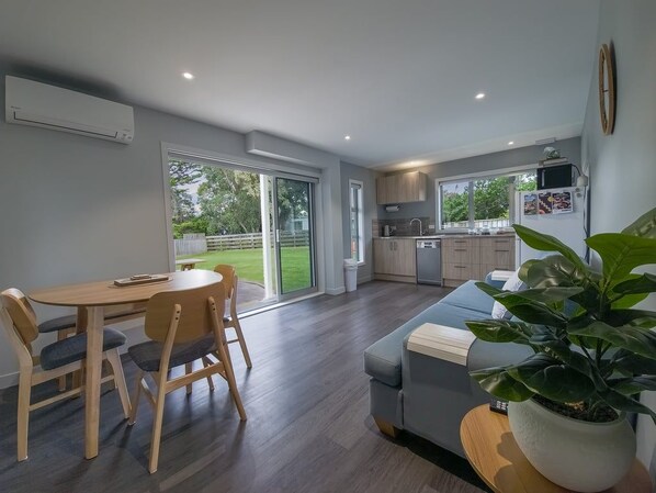 A modern kitchen with a dining area, a sofa, and a large potted plant.
