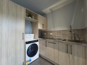 A compact kitchen with wooden cabinets, a built-in washing machine, and a stainless steel sink.