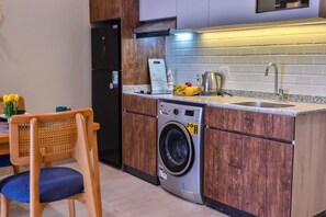 A compact kitchen with a built-in washing machine, a sink, and a countertop with fruits. - Luxury stay at Degla by Spacey #66 (Cairo)
