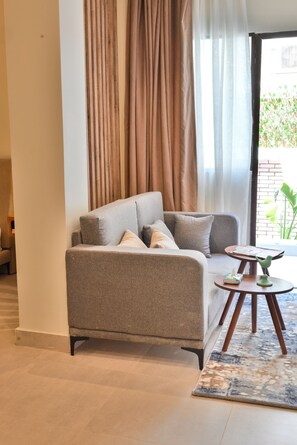 A modern living room with a grey sofa, a small round table, and a view through a window with curtains. - Luxury stay at Degla by Spacey #66 (Cairo)