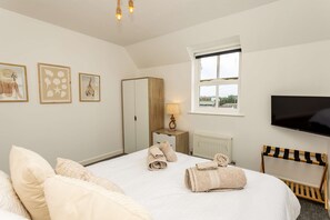 A hotel room with a bed, towels, a television, a window, and artwork on the wall. - 5 West -2 Bedroom House - Tenby (Tenby)