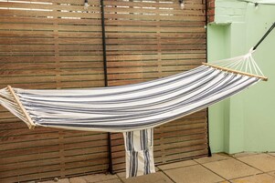 A hammock suspended between two wooden posts against a wooden fence and a green wall.