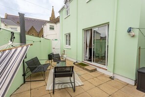 Eine Terrasse mit zwei Stühlen, einem kleinen Tisch, einer Hängematte und einer Glastür zu einem überdachten Bereich.