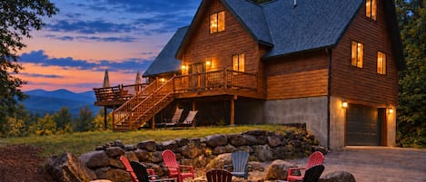 A two-story log cabin with a stone foundation, a balcony with outdoor seating, and a garage.