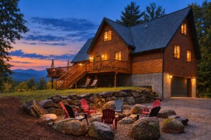 A two-story log cabin with a stone foundation, a balcony with outdoor seating, and a garage.