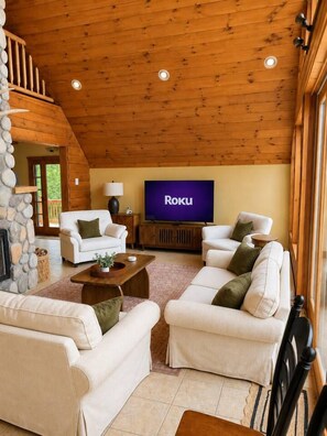 A cozy living room with a fireplace, white sofas, a TV, and a stone wall. - Luxury Retreat | Near Gore Mountain | Pets (North Creek)