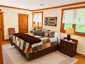 A bedroom with a large bed, a nightstand, a chair, and a window with curtains. - Luxury Retreat | Near Gore Mountain | Pets (North Creek)