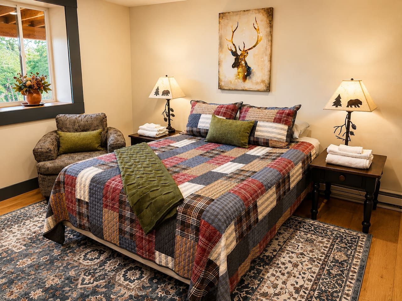 A bedroom with a large bed, two bedside tables, a chair, a window with a view, and a wall-mounted deer head artwork.
