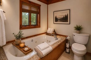 Un bagno con una vasca da bagno indipendente, un WC, una finestra con vista sugli alberi e un quadro appeso al muro.