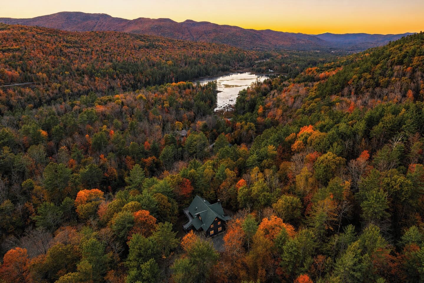Une cabane isolée, entourée d’une forêt dense, avec une rivière en arrière-plan.