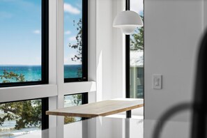 A room with large windows, a wooden shelf, and a white pendant light. - Luxury Home offering 100 feet of private, sandy beachfront on beautiful West Bay |  West Bay Haven (Traverse City)