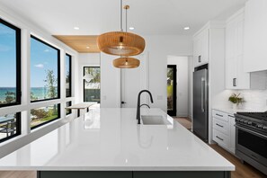 A modern kitchen with a large island, stainless steel appliances, and a view of the outdoors. - Luxury Home offering 100 feet of private, sandy beachfront on beautiful West Bay |  West Bay Haven (Traverse City)
