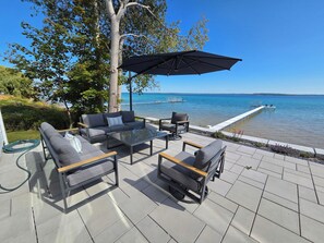 Eine Terrasse mit Gartenmöbeln, einem Glastisch und Blick auf das Wasser.