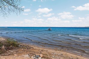 A beach with a pier extending into the water, a boat docked at the end, and a clear sky. - Luxury Home offering 100 feet of private, sandy beachfront on beautiful West Bay |  West Bay Haven (Traverse City)