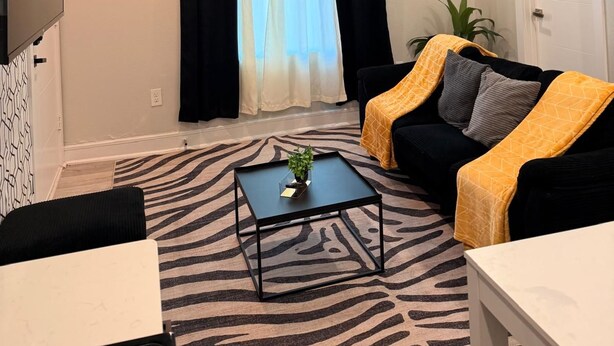 A living room with a black and white zebra-patterned rug, a black coffee table with a plant, a black sofa with a yellow throw, and a white door. - Enjoyable apartment at Dallas neighborhood (Dallas)