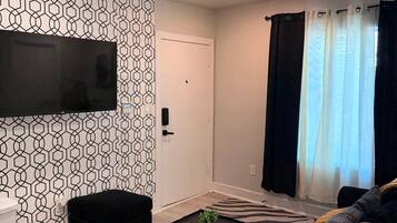 Un salon moderne avec un téléviseur à écran plat fixé au mur, un canapé noir, une petite table basse noire et un tapis à motifs zébrés.