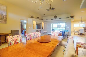 A spacious dining area with a large wooden table and patterned chairs, a sofa, and a chandelier. - Private Yard w/ Fire Pit & Pool! Cape Coral Escape (Cape Coral)