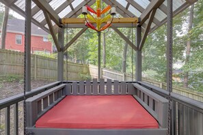 Een overdekt buitengebied met een rode, beklede zithoek, houten balkenplafond en uitzicht op een woonwijk.