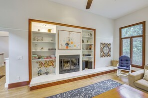 Een woonkamer met een open haard, boekenkasten, decoratieve voorwerpen en een blauwe fauteuil.