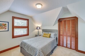 Une chambre à coucher comprenant un lit, une table de chevet, une lampe, une fenêtre avec des stores et une porte à panneaux ajourés.