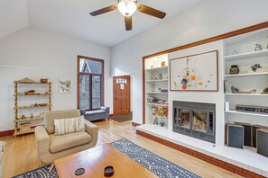 A living room with a sofa, coffee table, and a fireplace. There is a bookshelf with decorative items and a window with blinds. - Chattanooga Home w/ Treetop Deck & Yard! (Chattanooga)