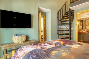 A bedroom with a large bed, a television mounted on the wall, a wooden bench, and a staircase leading to an upper level. - Walk to Ski & Main St! Newly Refinished w/ Hot Tub (Breckenridge)
