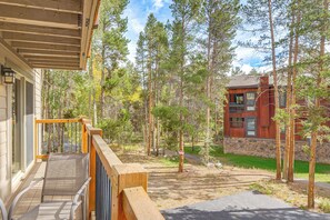 A wooden deck with a metal railing, a stone wall, and a building with large windows and a stone foundation. - Walk to Ski & Main St! Newly Refinished w/ Hot Tub (Breckenridge)