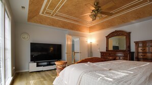 Una camera da letto con un letto grande, una televisione, un comò in legno e una ventola a soffitto.