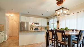 A modern kitchen with white cabinetry, a stainless steel refrigerator, a microwave, and a dining area with wooden chairs and a table.