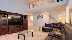 A spacious living room with a large flat-screen TV, leather sofa, and a glass coffee table.