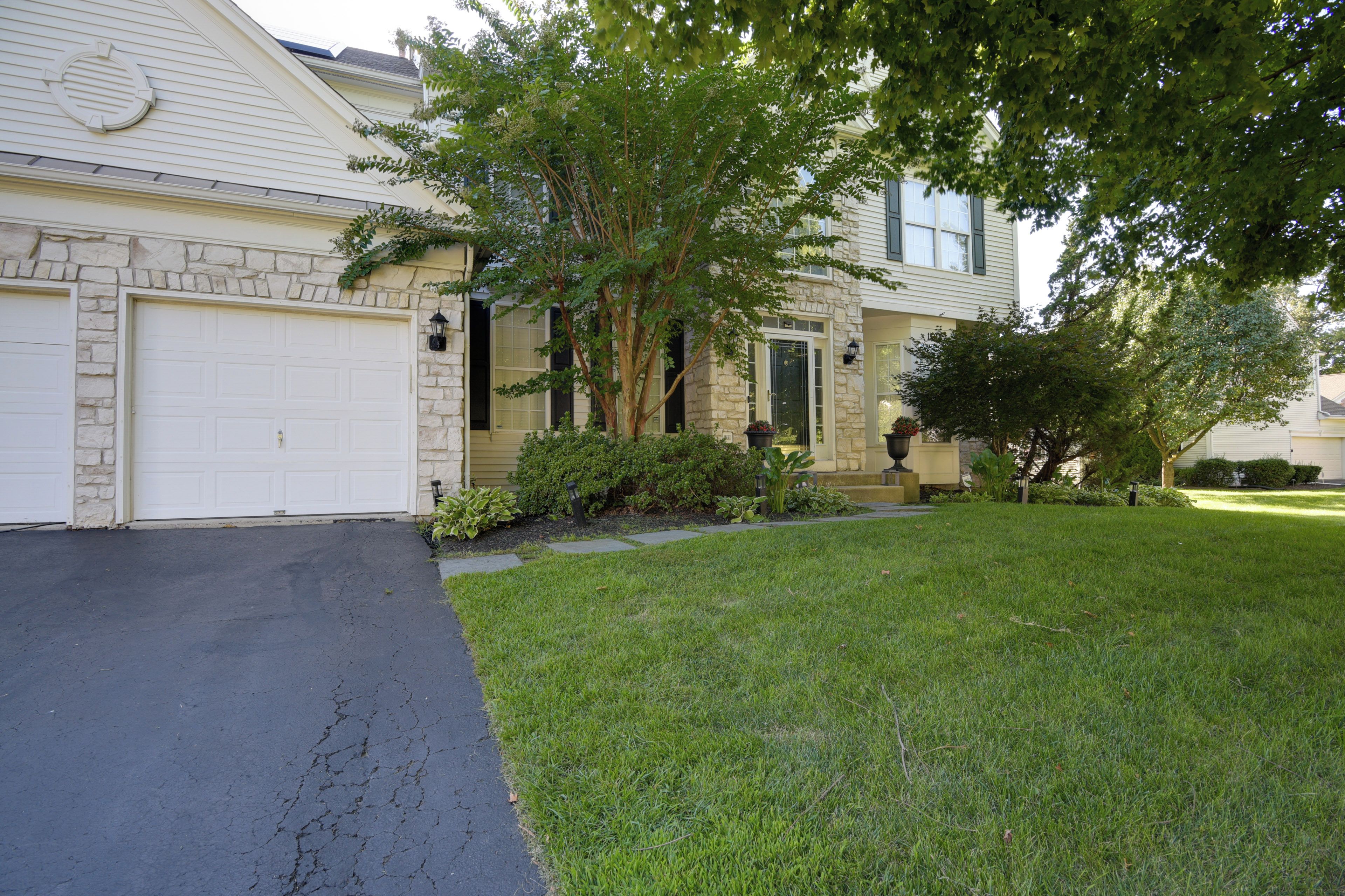 A two-story house with a garage, stone facade, and a well-maintained lawn.