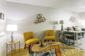 Een woonkamer met twee gele fauteuils, een salontafel, een eettafel met een kom, en decoratieve wandkunst.